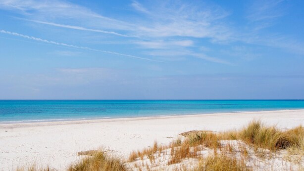 Una platja de sorra blanca i aigua blava cristal·lina sota un cel serè.