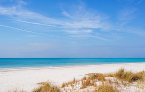 Ein Strand mit weißem Sand und klarem, blauem Wasser unter blauem Himmel.