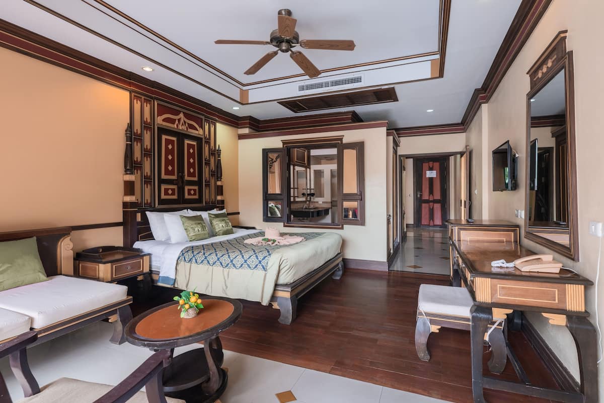 A hotel room with a bed, a sitting area with a table, a vanity with a mirror, and a ceiling fan.