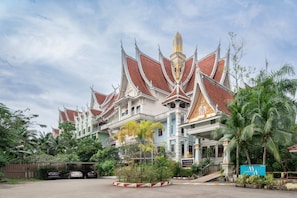 Un bâtiment traditionnel thaïlandais doté d’une architecture richement décorée, d’une entrée fermée par un portail et d’un espace de stationnement.
