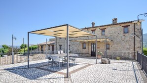 Un bâtiment en pierre doté d’un patio comprenant une table et des chaises, le tout abrité par une marquise.