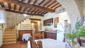 Une cuisine rustique avec des poutres en bois, un escalier en pierre et un coin repas comprenant une table et des chaises.