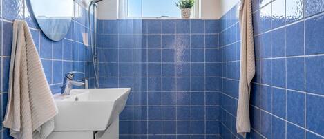 A bathroom with blue tiles, a white sink, a mirror, a shower, and a window with a plant.
