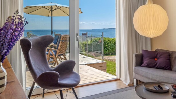 En moderne stue med havudsigt, en terrasse med udendørs møbler og en hængende lampe.