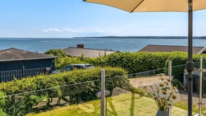 En balkon med udsigt over havet, en parkeret bil og en bygning i baggrunden.