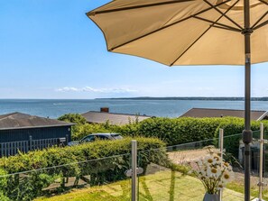Ein Balkon mit Blick auf das Meer, ein geparktes Auto und ein Gebäude im Hintergrund.