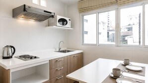 A modern kitchen with a stove, kettle, microwave, and sink. There is a dining table with plates and cups. - Suk41 (Bangkok)