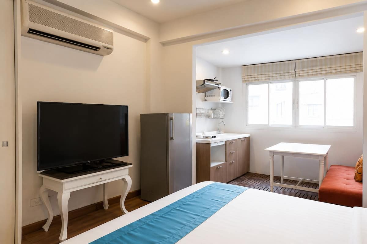 Habitación de hotel compacta con televisión, refrigerador, kitchenette y una cama con colcha azul.