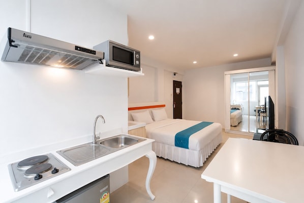 A compact hotel room with a kitchenette, a bed with a blue accent, a TV, and a bathroom. - Suk41 (Bangkok)