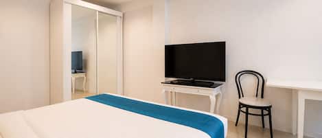 A hotel room with a bed, a desk with a TV, and a chair.