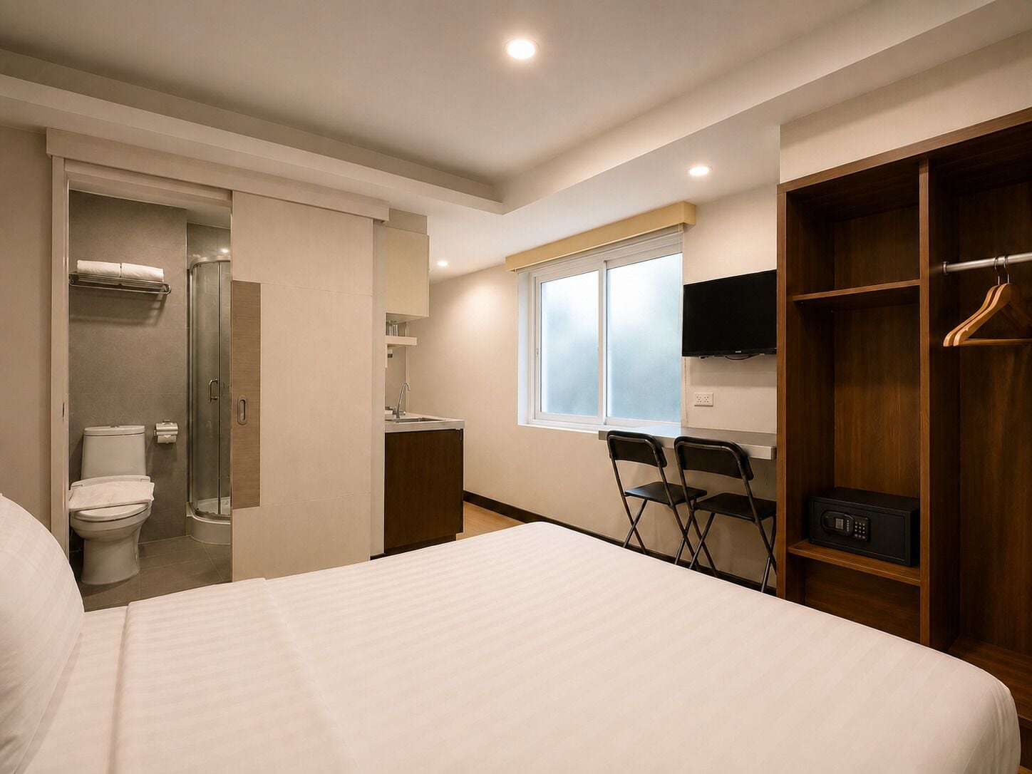 A hotel room with a bed, a shower, a sink, a TV, and a wardrobe.