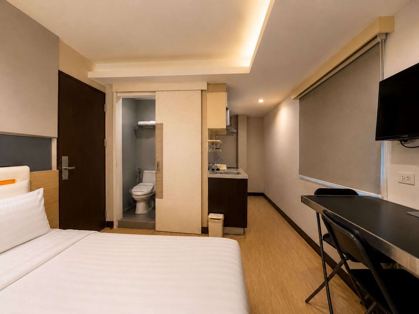 A hotel room with a bed, a bathroom, a sink, and a TV.