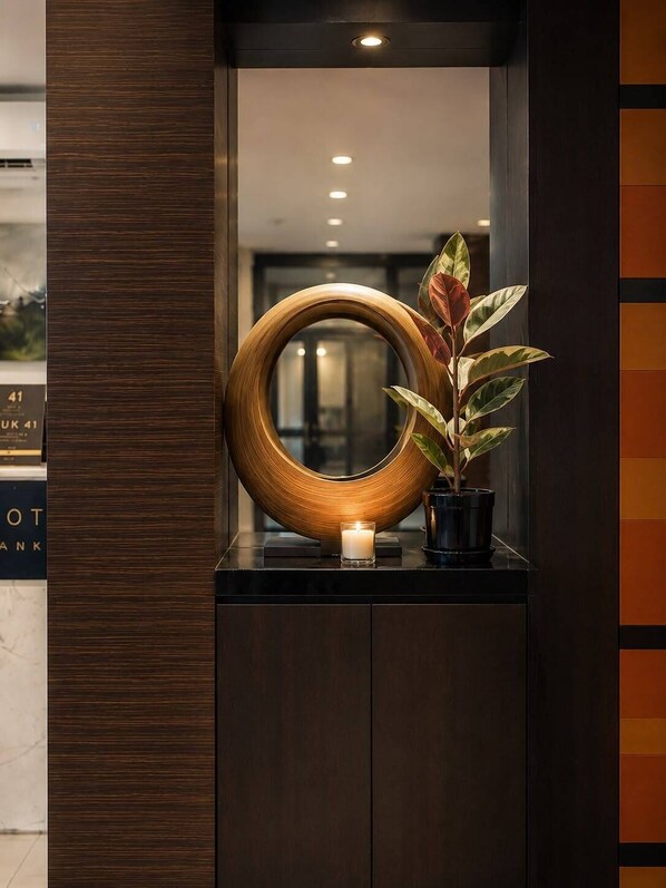 A reception area with a wooden circular mirror, a potted plant, and a lit candle on a dark counter. - Suk41 (Bangkok)