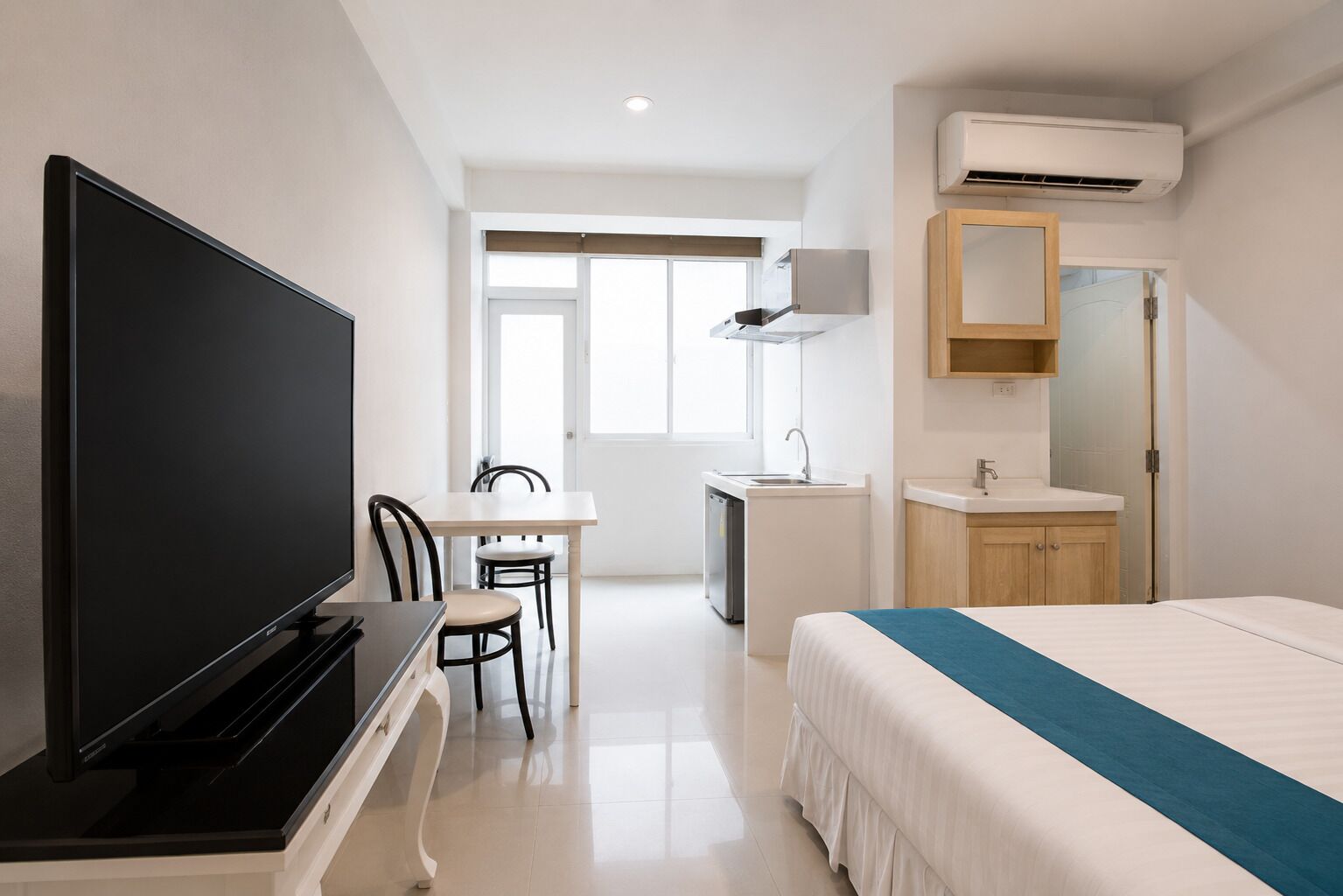 A hotel room with a bed, a TV, a desk with a chair, a bathroom with a sink and mirror, and a window.