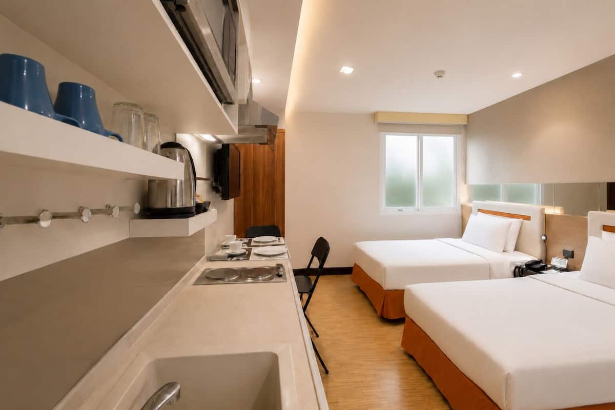 Habitación de hotel con kitchenette, dos camas, ventana y zona de ducha.