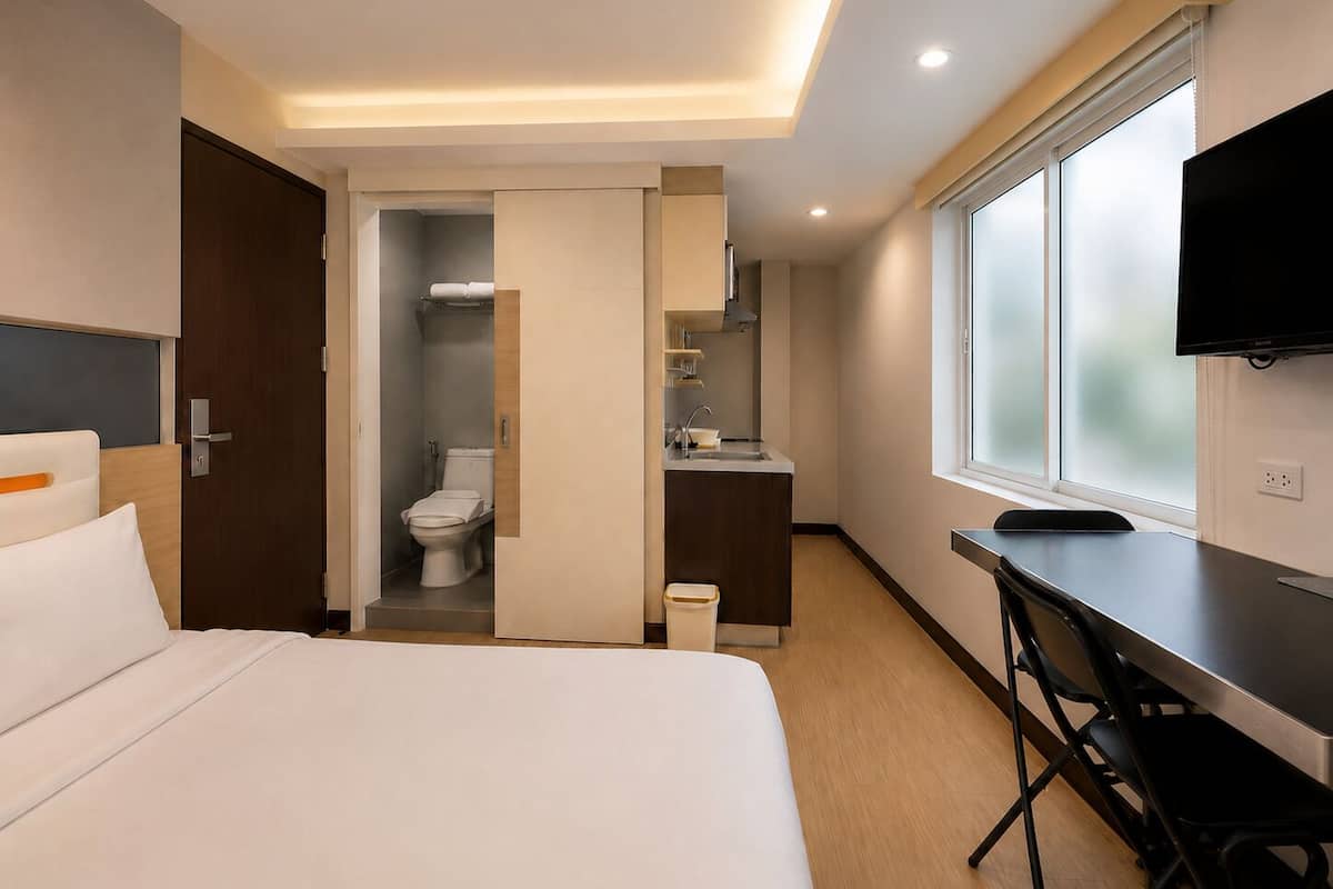 Una habitación de hotel con cama, escritorio, televisión, baño y ventana.
