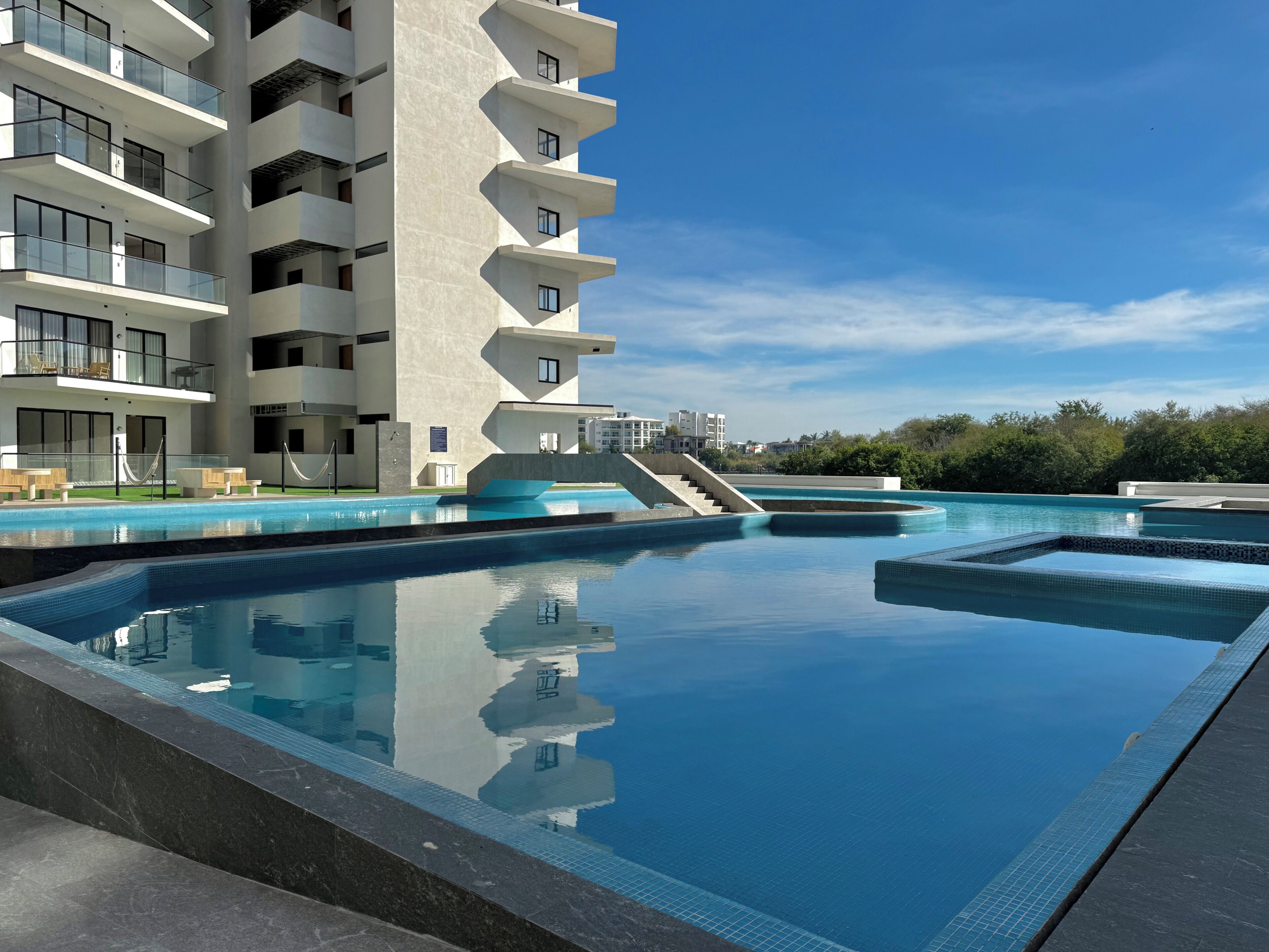 A modern hotel with a swimming pool, outdoor seating, and a staircase leading to the upper floors.