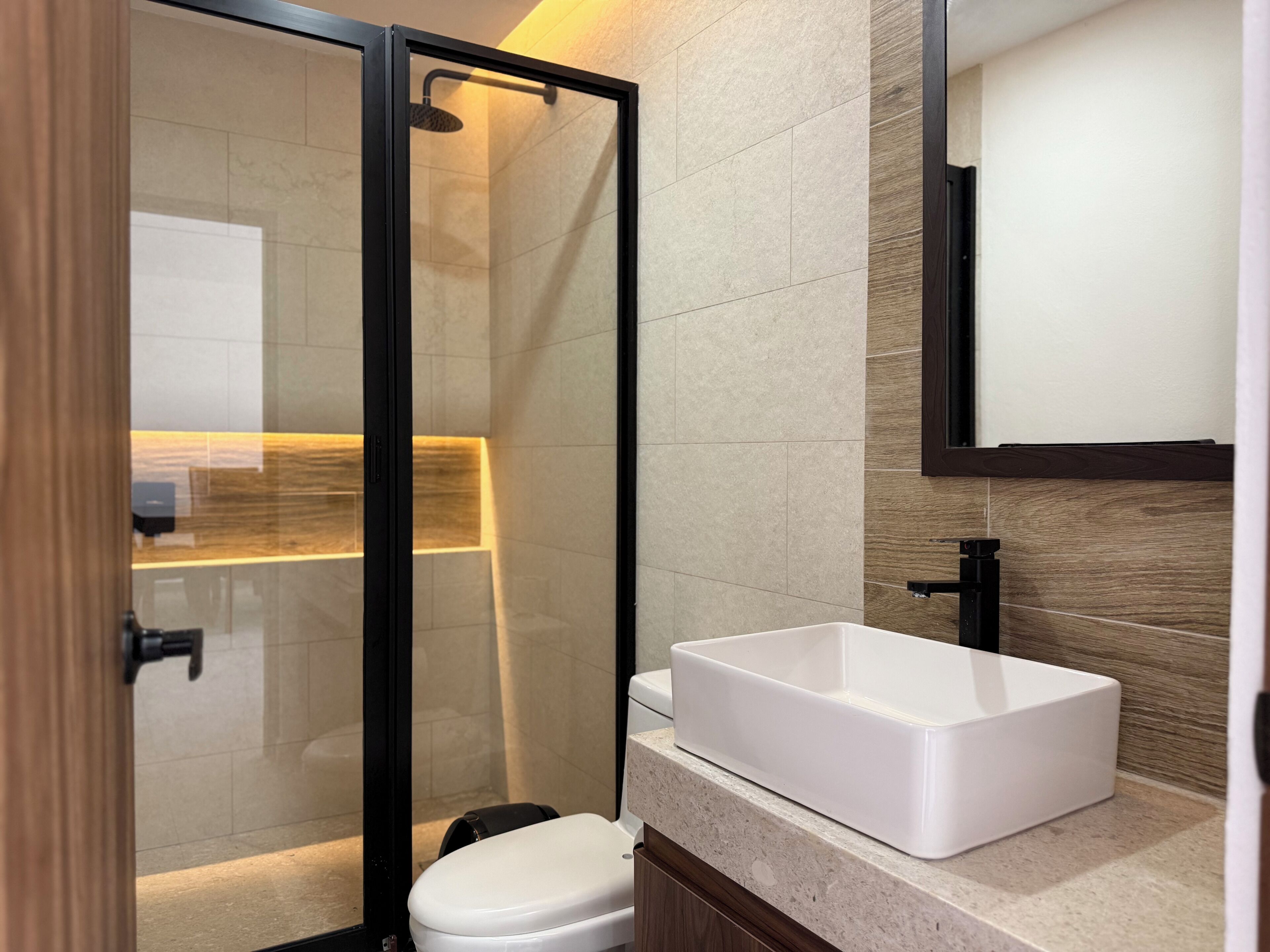 A modern bathroom with a glass-enclosed shower, a white sink, and a wooden vanity.