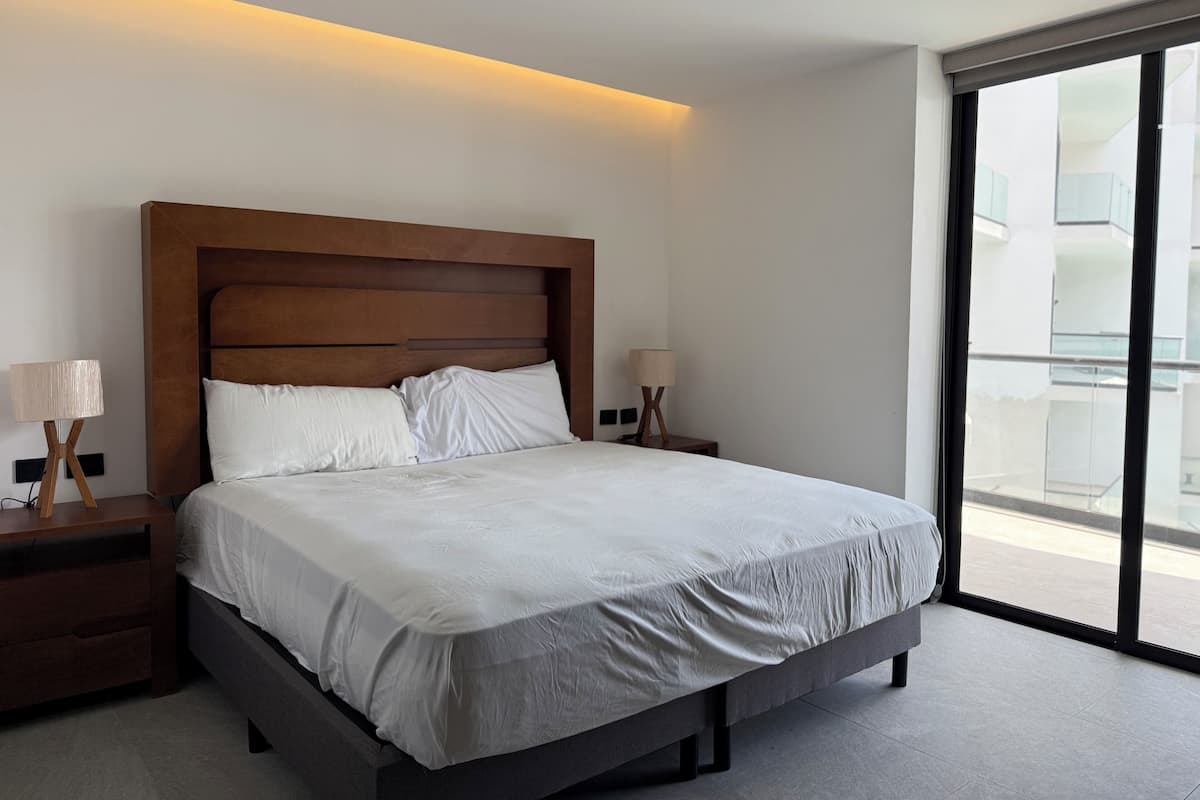 Habitación de hotel moderna con una cama grande, dos mesitas de noche y vistas al balcón exterior.