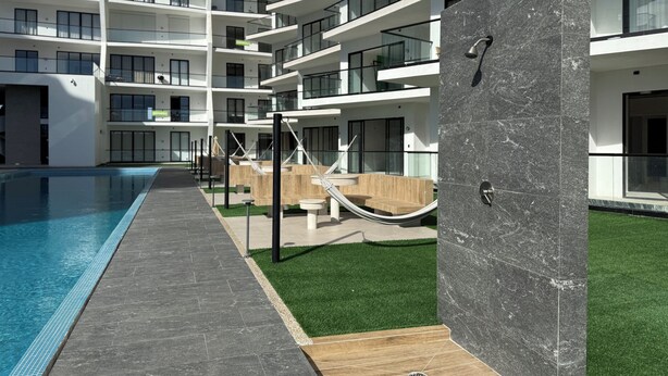 A modern building with multiple balconies, a swimming pool, and outdoor seating areas.