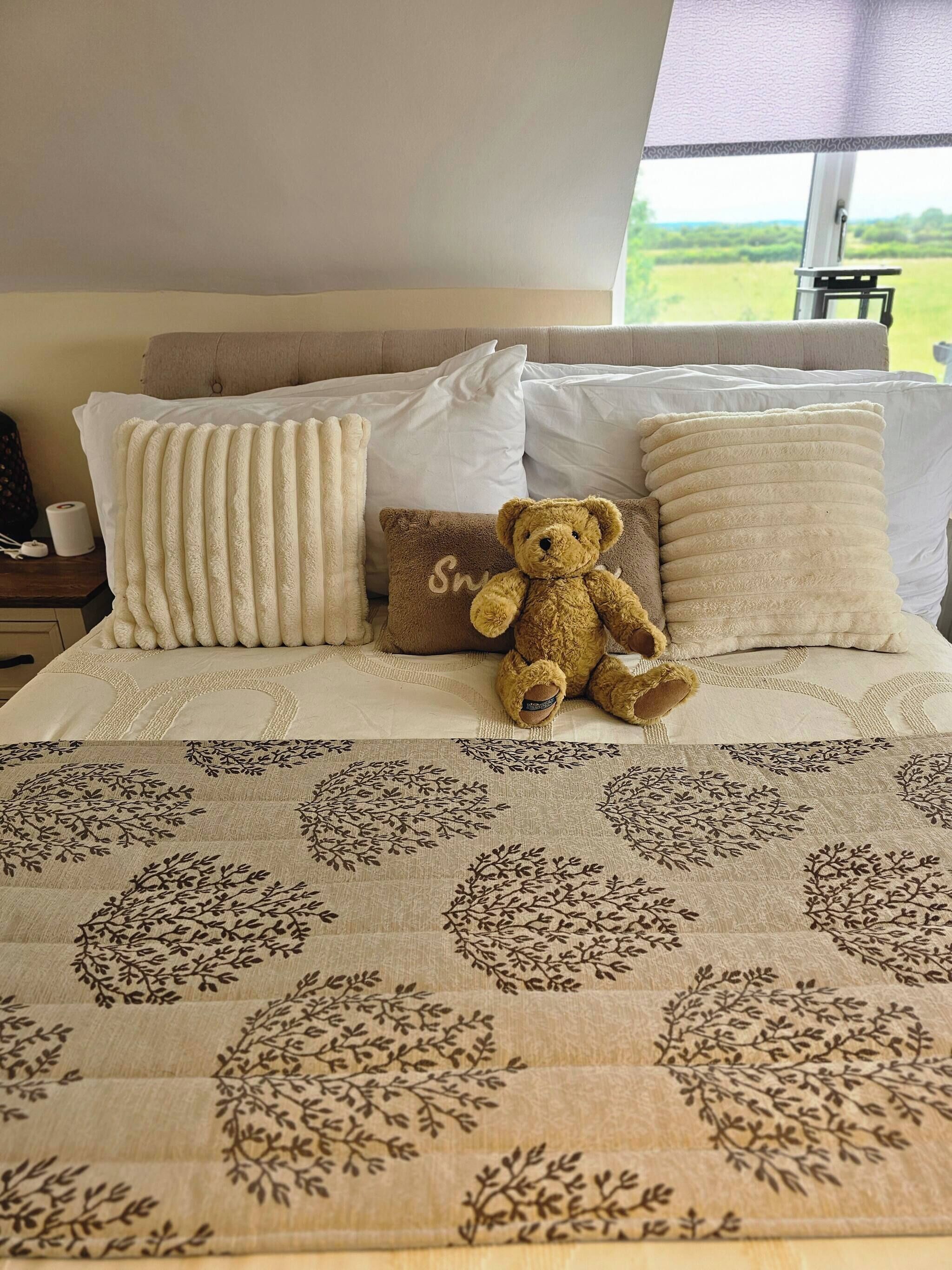 A bed with a teddy bear, pillows, and a patterned bedspread.