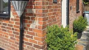 Een bakstenen gebouw met een bloembak aan de gevel, een deur en een struik.