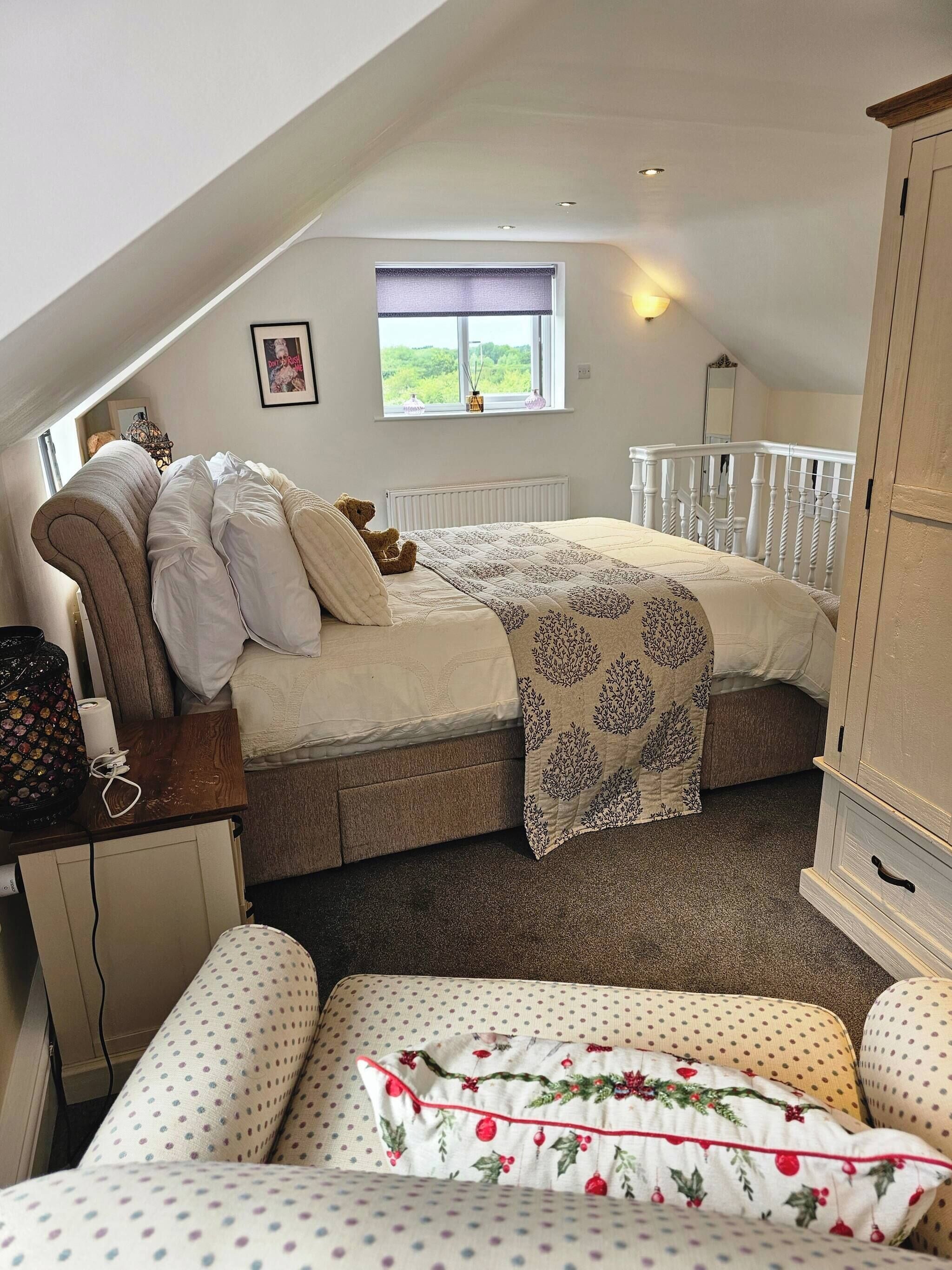 Ein gemütliches Schlafzimmer unter dem Dach mit Bett, Kommode, Fenster mit Blick und einem Sessel.