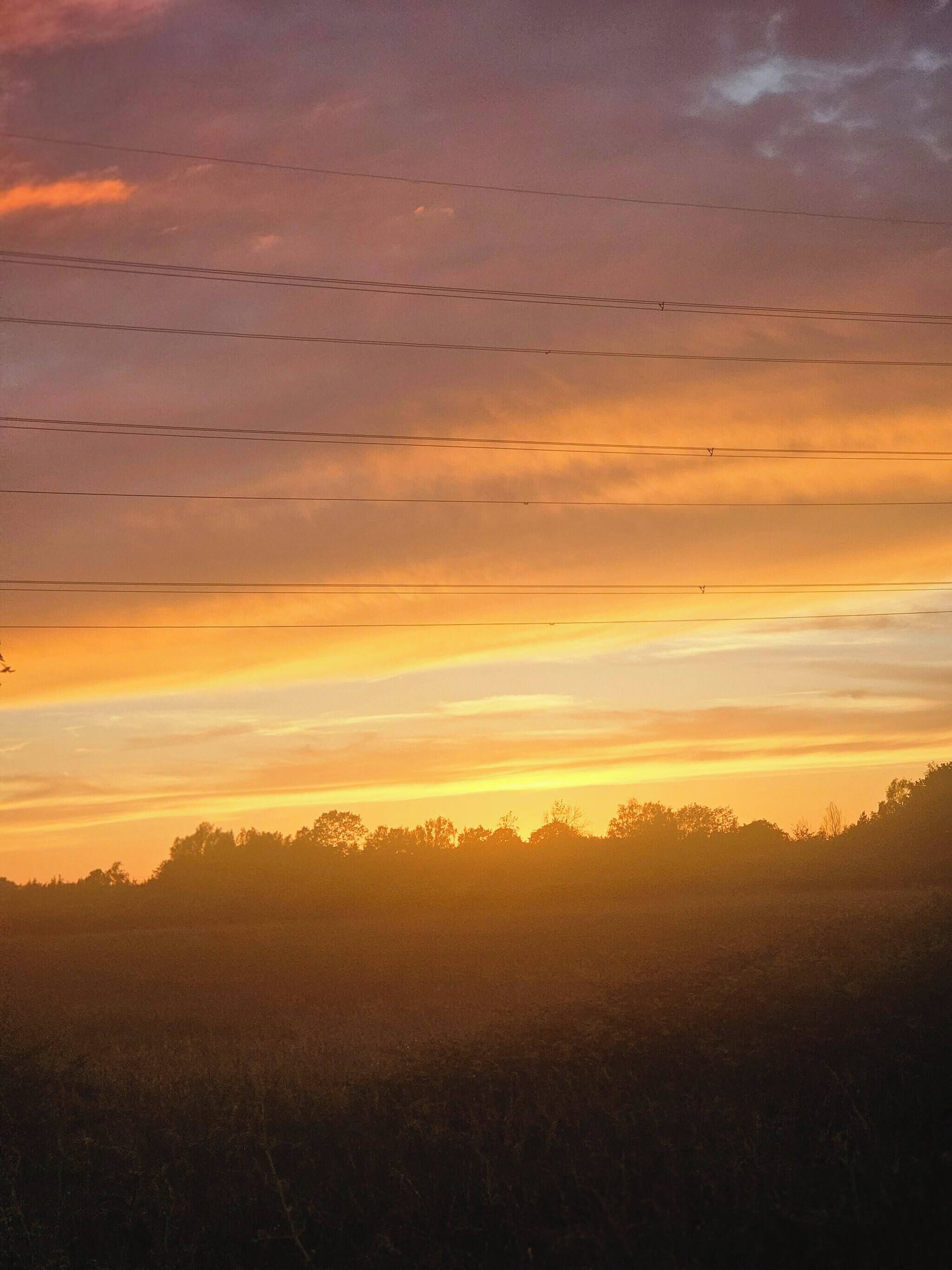A sunset over a landscape with power lines.