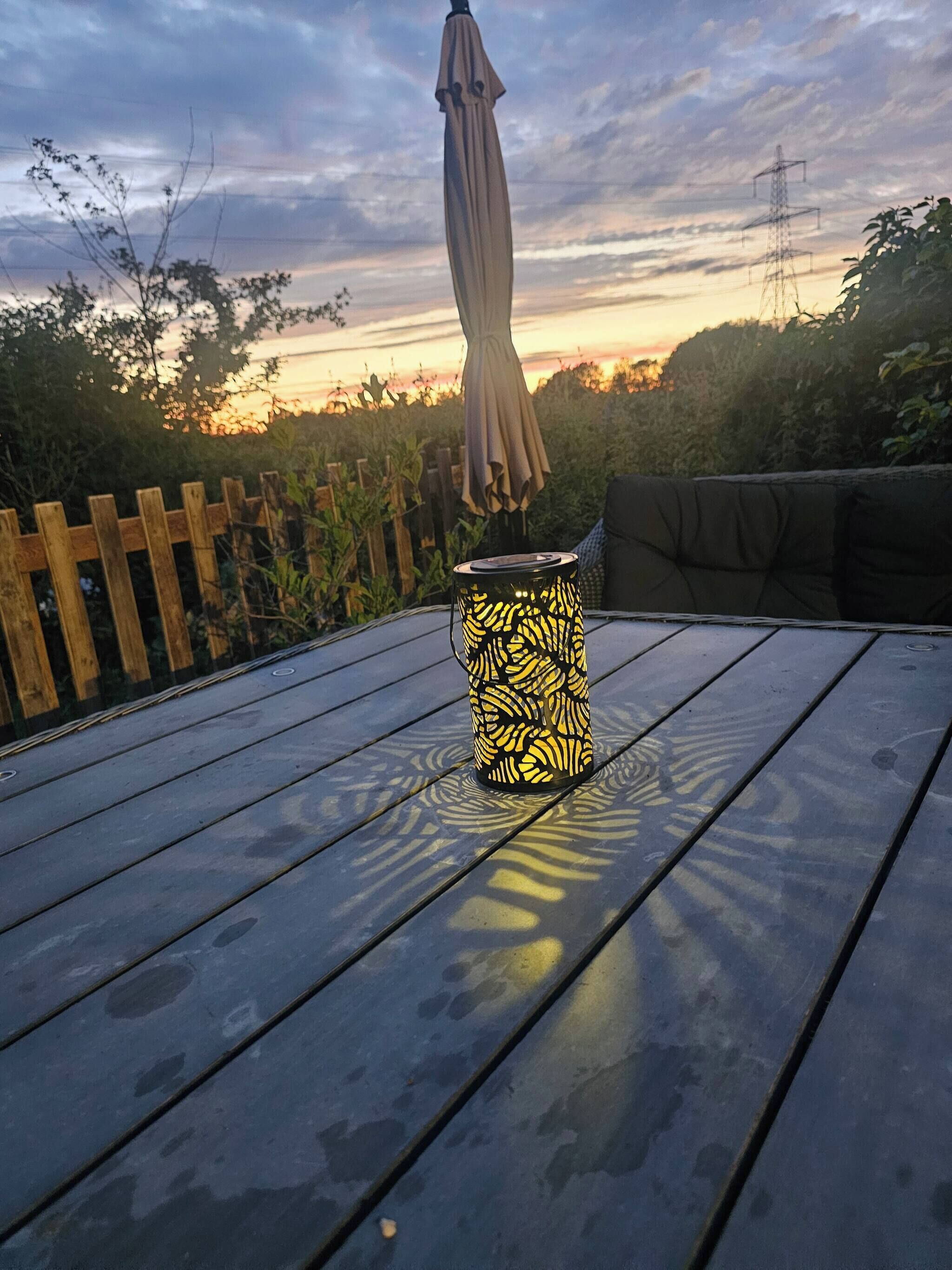 Una mesa con un farol estampado y un paraguas, frente a un atardecer.