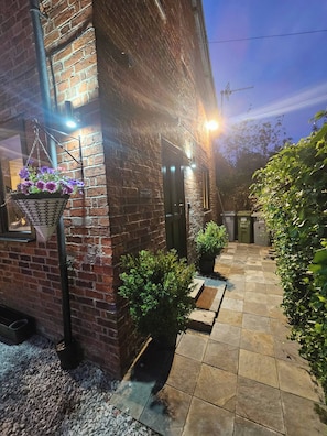 A brick building with a tiled patio, a hanging flower basket, and a door. - A Romantic Retreat in a Stunning Setting (Newark)