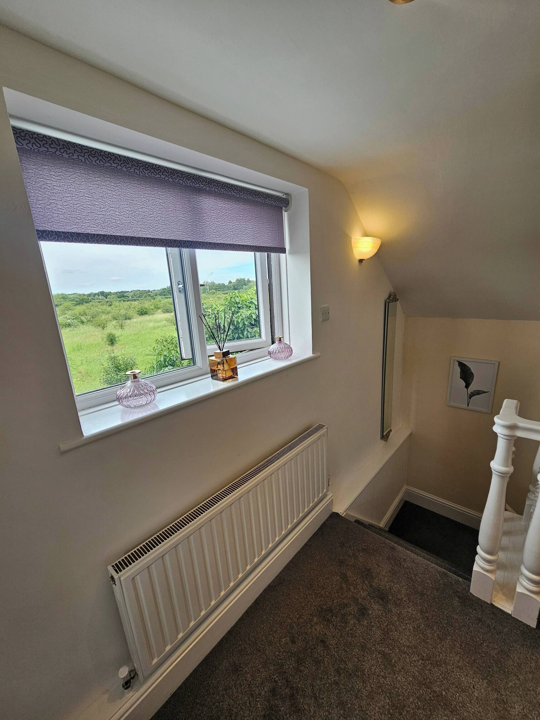 A room with a large window, a radiator, a staircase, and a wall-mounted light fixture.