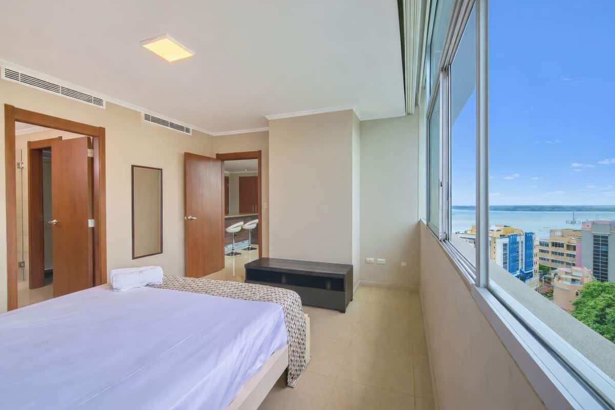 Een hotelkamer met een bed, een zithoekje, een spiegel en een raam met uitzicht op de stad.