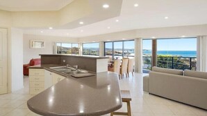 A modern kitchen with a central island, dining area with chairs, and a sofa. - Kyeema (Bega Valley)