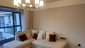 Una sala de estar moderna con un sofá seccional, una araña, un ventanal grande y un enchufe en la pared.