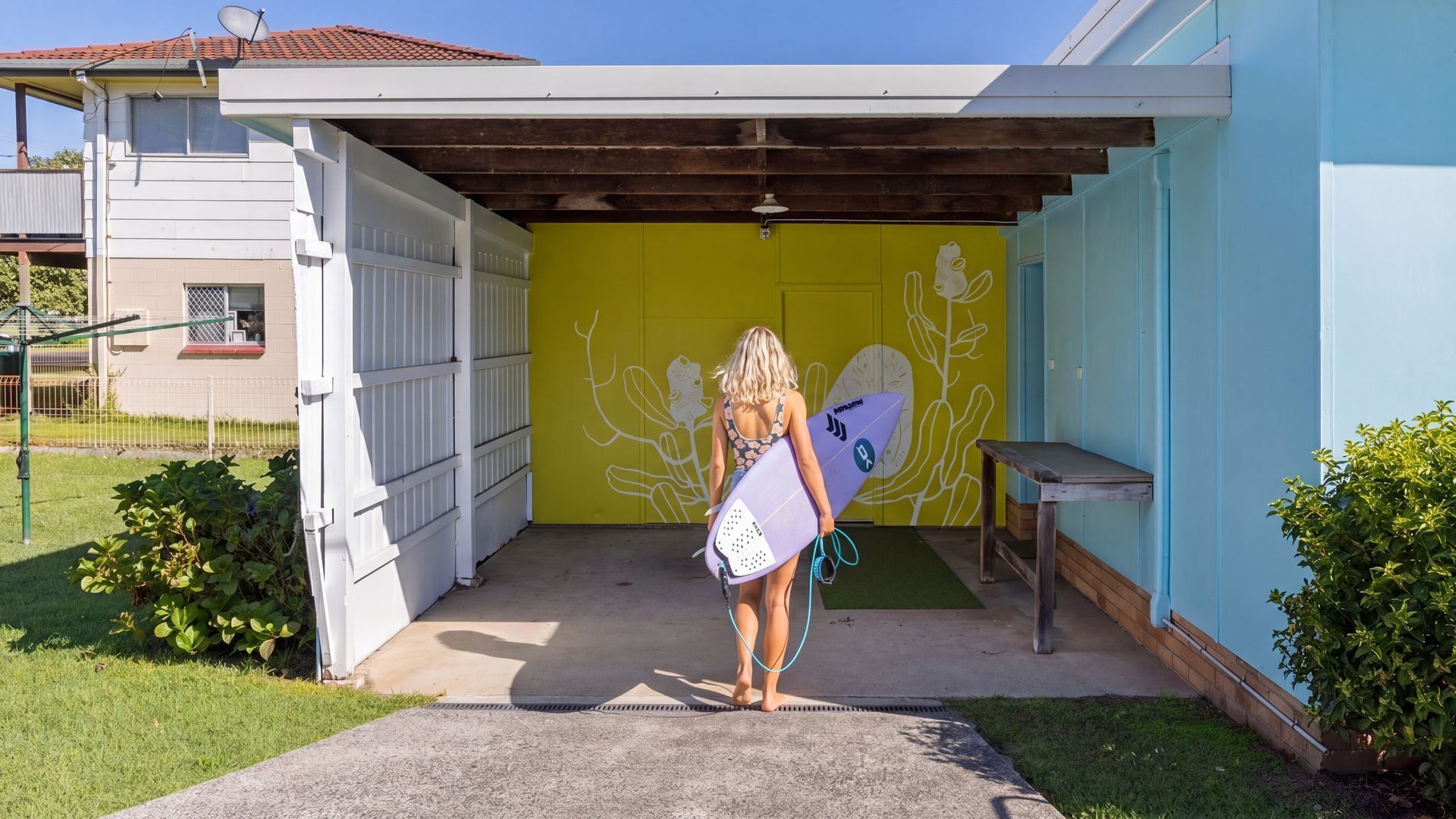 A covered outdoor area with a concrete floor, a bench, and a wall with a plant mural.