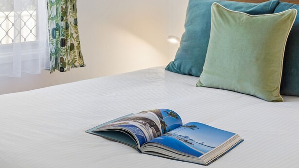 A bed with a white sheet, a green pillow, and an open magazine on it. - Little Banksia  - Pet-Friendly in the Heart of Yamba - Holiday Yamba (Yamba)