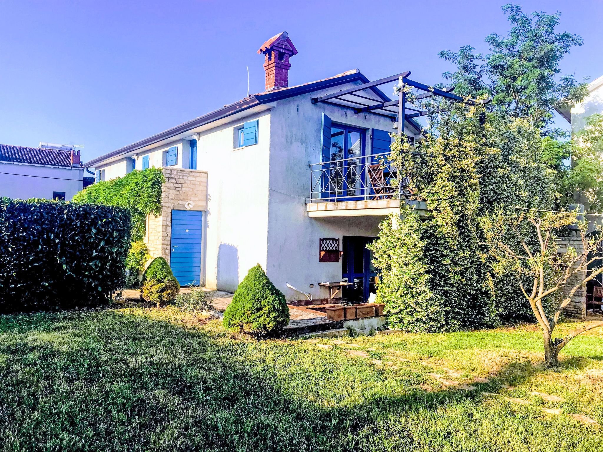 Un bâtiment à deux étages doté d’un balcon, d’une porte bleue et d’un petit jardin.