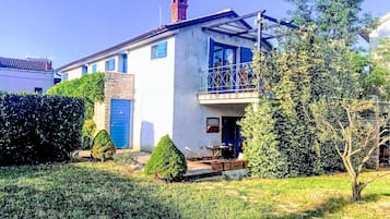 Un bâtiment à deux étages doté d’un balcon, d’une porte bleue et d’un petit jardin.