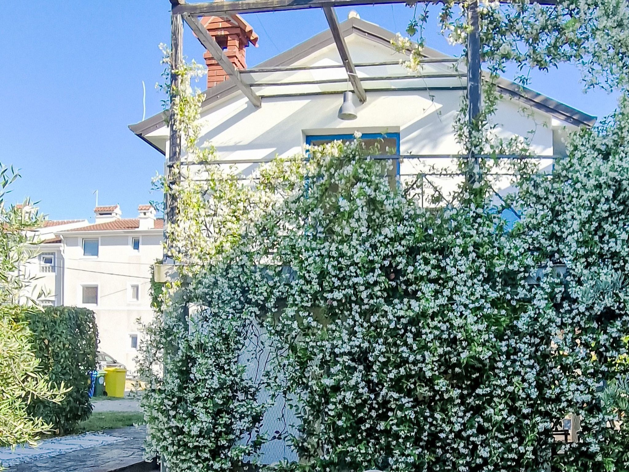 Un edificio residencial con fachada blanca, chimenea visible y un jardín con plantas de flores blancas.