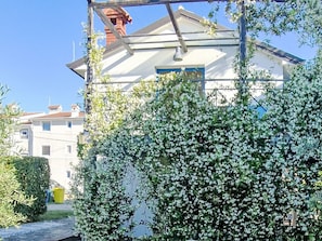 En bostadsbyggnad med en vit fasad, en synlig skorsten och en trädgård med vita blommande växter.