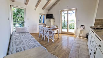 Una habitación con cama, una mesa de comedor con sillas, una cocina y un ventanal corredizo que da a un jardín.