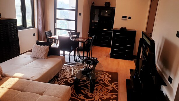 A modern living room with a sofa, a dining table with chairs, a TV, and a kitchen area with cabinets. - Peaceful and secure Kyanja Oasis with Modern Amenities & Hot Shower (Kampala)