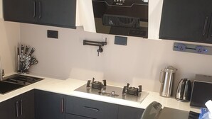 A modern kitchen with black cabinets, a built-in oven, a sink, and a water dispenser. - Peaceful and secure Kyanja Oasis with Modern Amenities & Hot Shower (Kampala)