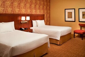 Ein Hotelzimmer mit zwei Betten, einem Nachttisch mit Telefon und Lampe, einem roten Sessel und gerahmten Bildern an der Wand.