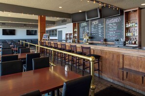 Ein Restaurantinneres mit Barbereich, Holztischen und schwarzen, gepolsterten Stühlen.