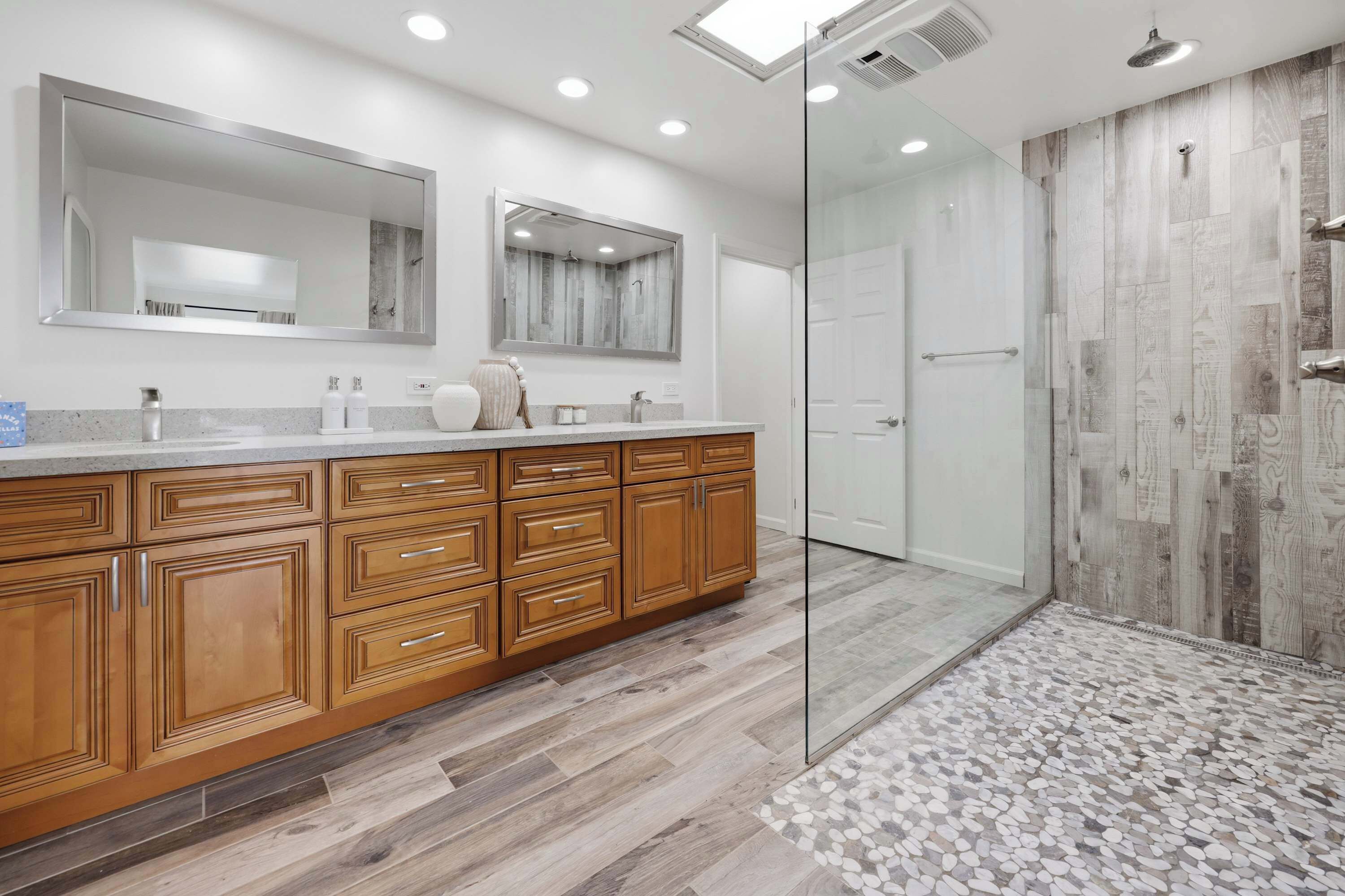 A modern bathroom with a wooden vanity, large mirrors, and a glass shower enclosure.