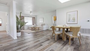 Een moderne woonkamer met een eethoek, houten vloeren, witte muren en een groot raam.
