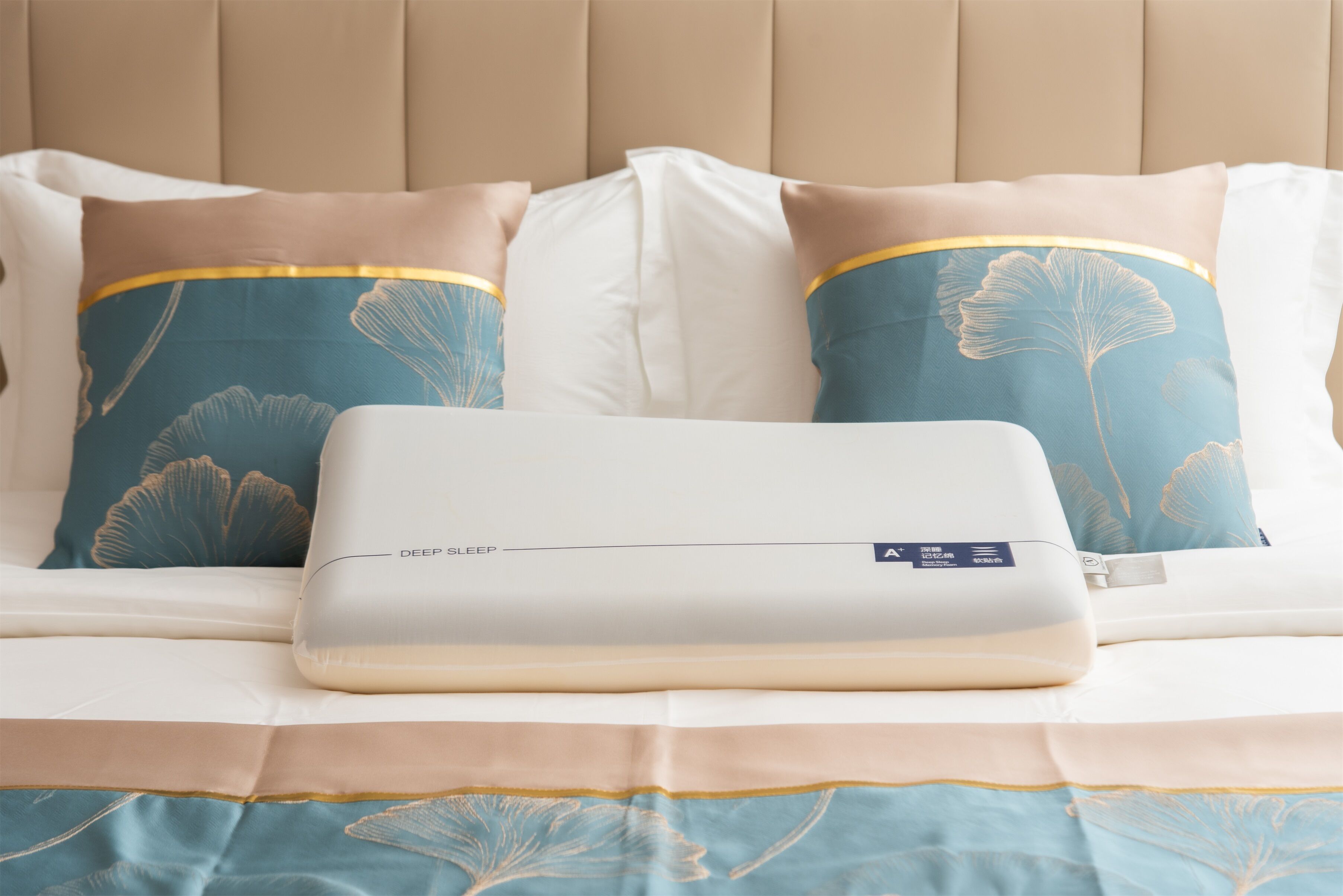 A bed with a white mattress, beige headboard, and decorative pillows with a blue and gold pattern.