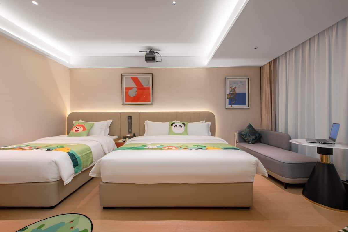 Ein Hotelzimmer mit zwei Betten, einem Schlafsofa, einem Schreibtisch mit einem Laptop und Kunstwerken an den Wänden.