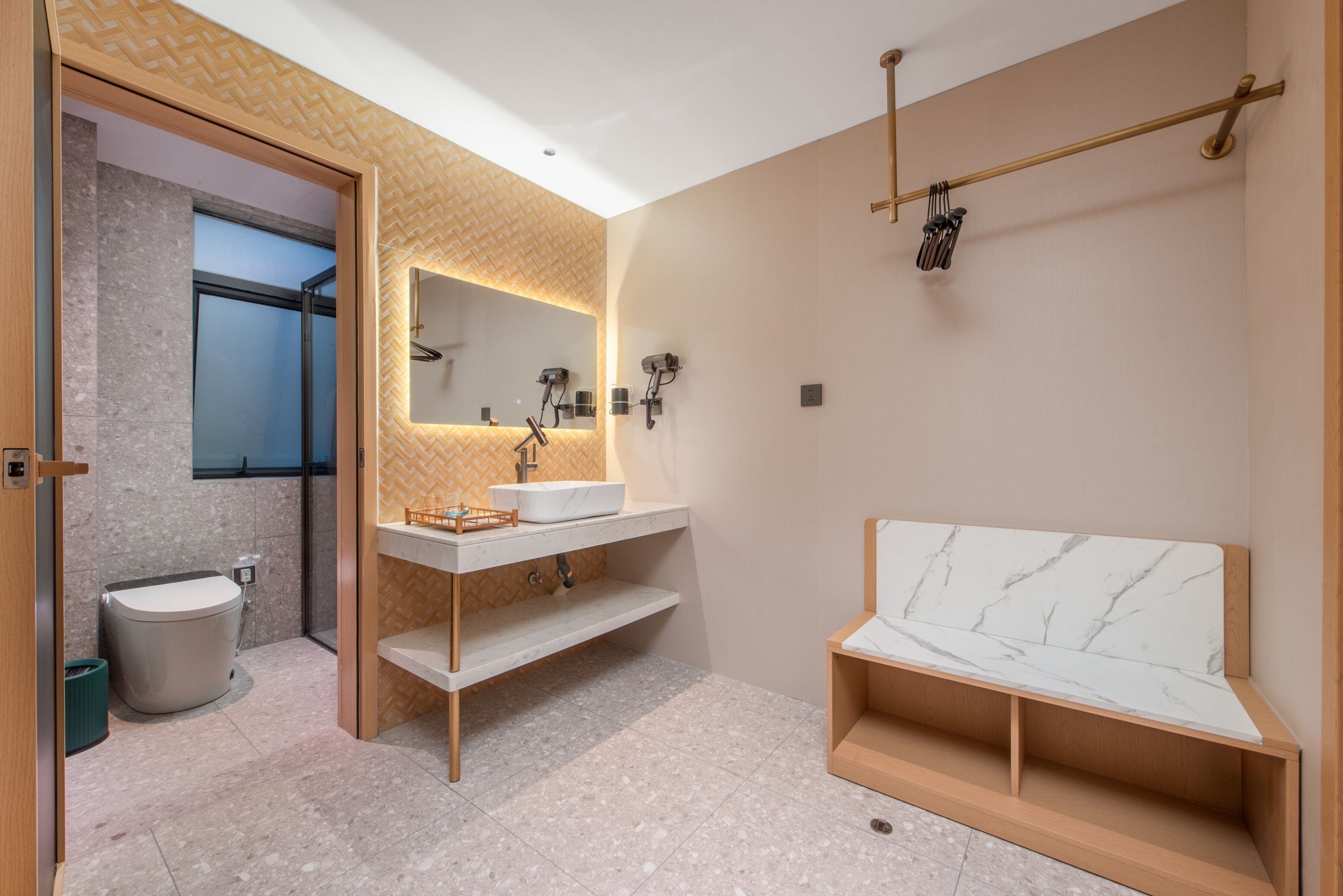 Un baño moderno con inodoro, lavamanos, espejo, ducha y una banqueta.